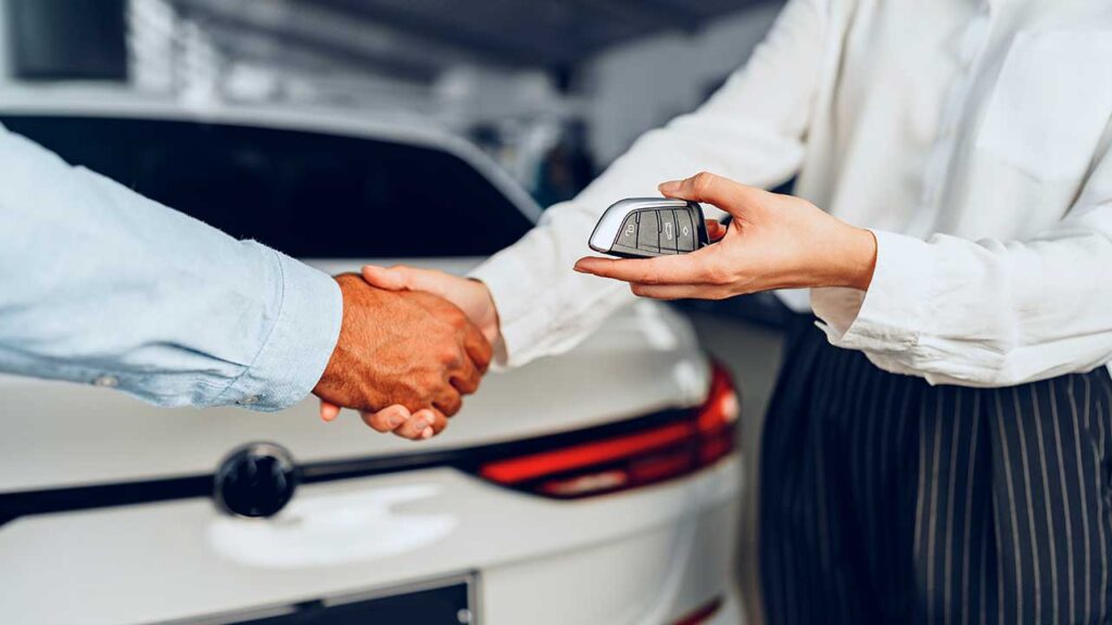 5 razões para usar a InstaCarro e vender seu carro rápido 7 Imagem de um homem e uma mulher se cumprimentando com aperto de mãos e entregando uma chave canivete. Um carro branco ao fundo. vender carro pessoa física