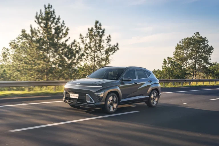 Lançamentos 4 Hyundai Novo KONA Hybrid em movimento em estrada cercada por árvores, sob céu limpo